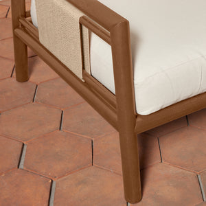 Close-up of an armchair with a brown frame, white cushions, and a beige woven throw, set on terracotta hexagonal tiles. - Number 7