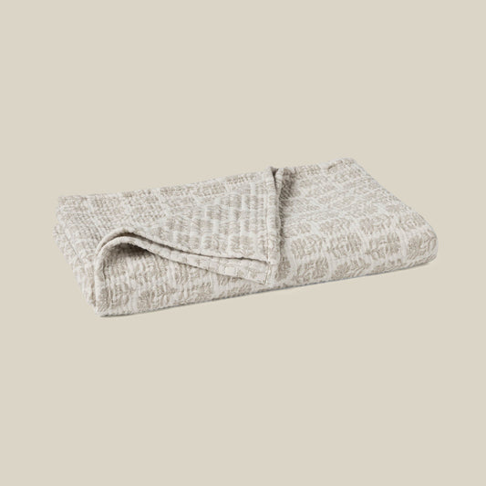 A folded textured blanket in a light beige and gray pattern, shown on a solid beige background.