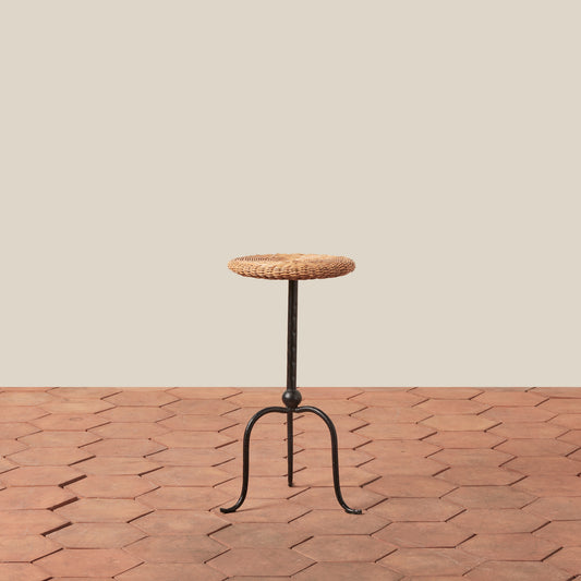 Small round table with woven top and metal legs on a wooden floor.