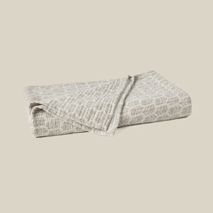 A folded textured blanket in a light beige and gray heathered pattern, set against a solid beige background. - Number 1