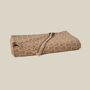 A folded brown blanket with a textured, woven abstract pattern, displayed on a solid light beige background. - Number 1