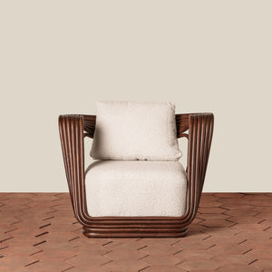 A modern accent chair with a dark brown ribbed frame and textured cream bouclé seat and back cushions, set against a neutral beige wall and brown herringbone wood floor. - Number 5