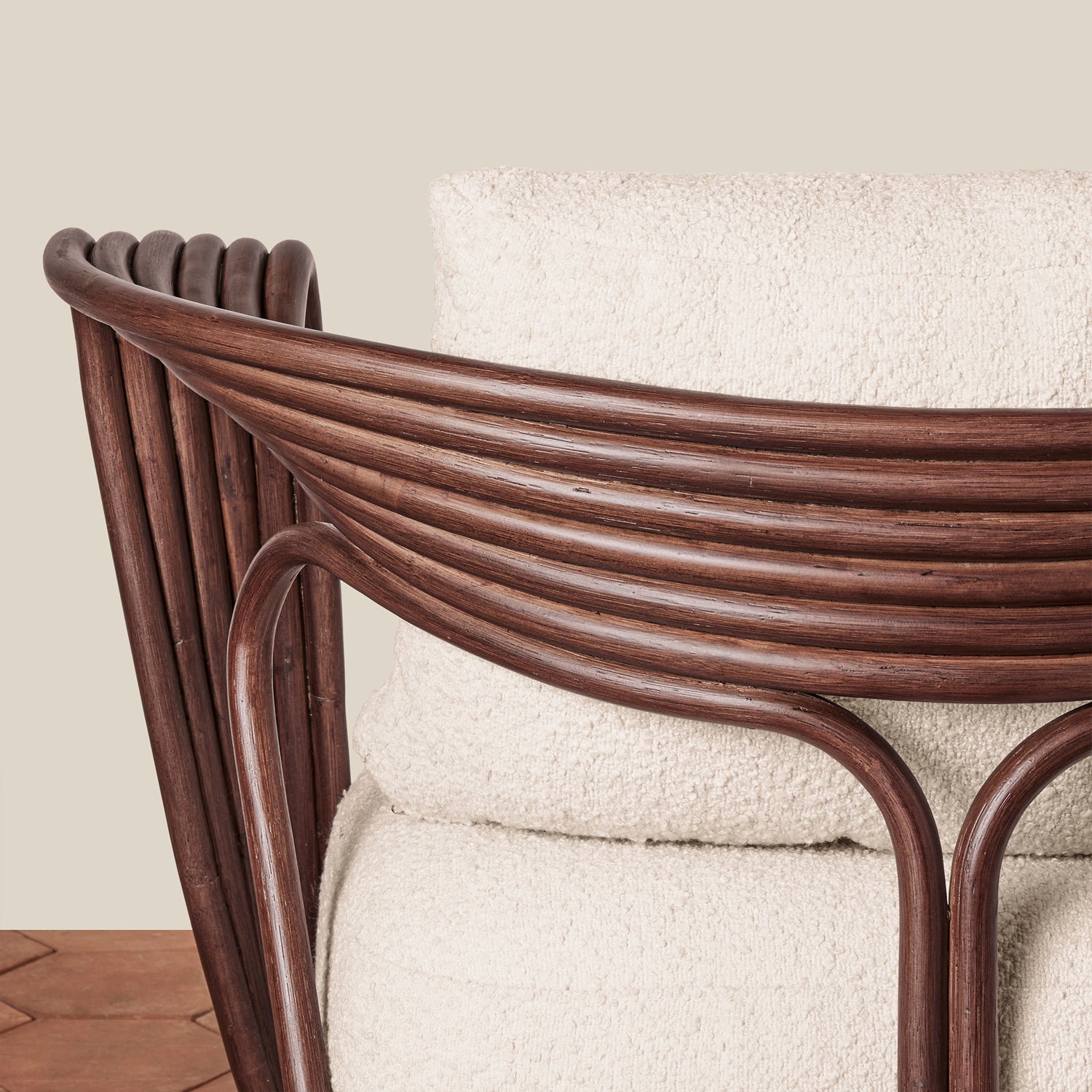 A modern armchair with a dark brown wicker frame and textured off-white bouclé cushions, set against a neutral beige wall and brown herringbone wood floor.- Number 8