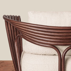 A modern armchair with a dark brown wicker frame and textured off-white bouclé cushions, set against a neutral beige wall and brown herringbone wood floor. - Number 8