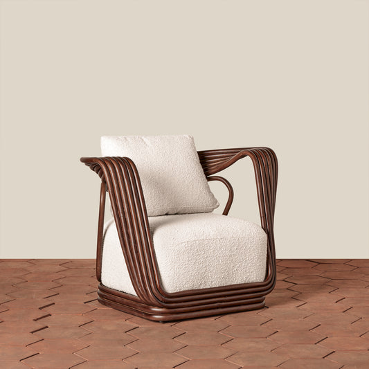 A modern armchair with a dark brown wicker frame and textured off-white bouclé cushions, set against a neutral beige wall and brown herringbone wood floor.