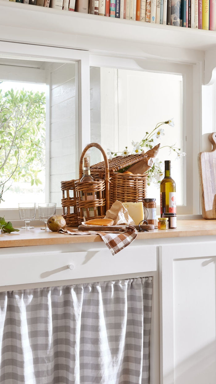 Kitchen counter with baskets, fruits, and a bottle of wine near a window.