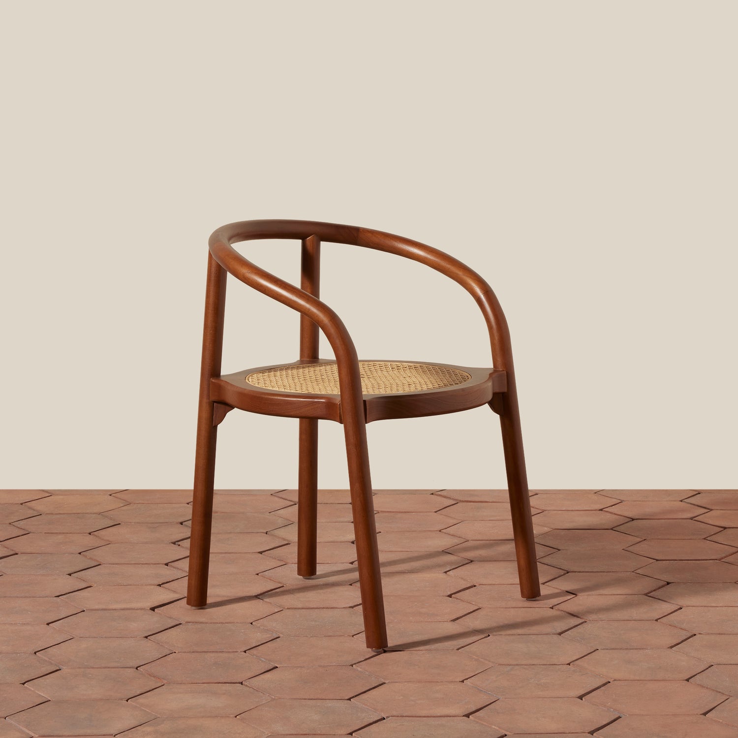 A mid-century modern wooden dining chair with a curved armrest, brown bentwood frame, and a woven cane seat, set against a beige wall and terracotta hexagonal tile floor.- Number 7