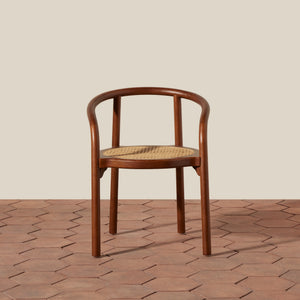 A bentwood dining chair with a warm brown wood frame and a natural woven cane seat, positioned against a neutral beige wall and terracotta hexagonal tile floor. - Number 9