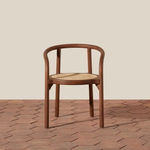 A modern wooden chair with a curved backrest and a woven cane seat, shown on a terracotta hexagonal tile floor against a solid beige background. - Number 3