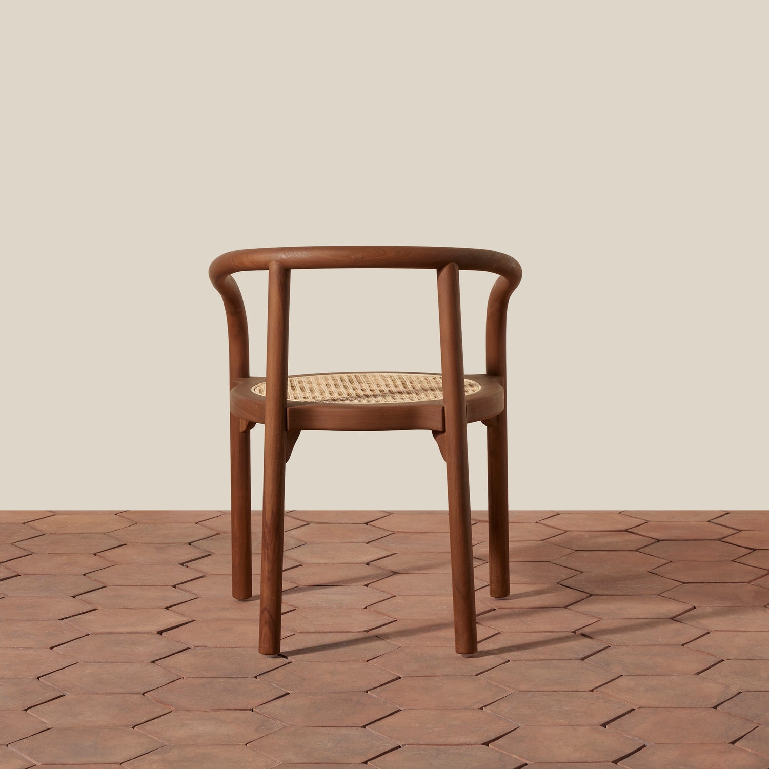 A mid-century modern wooden chair with a curved backrest and woven cane seat, positioned on a terracotta hexagonal tile floor against a solid beige background.- Number 4
