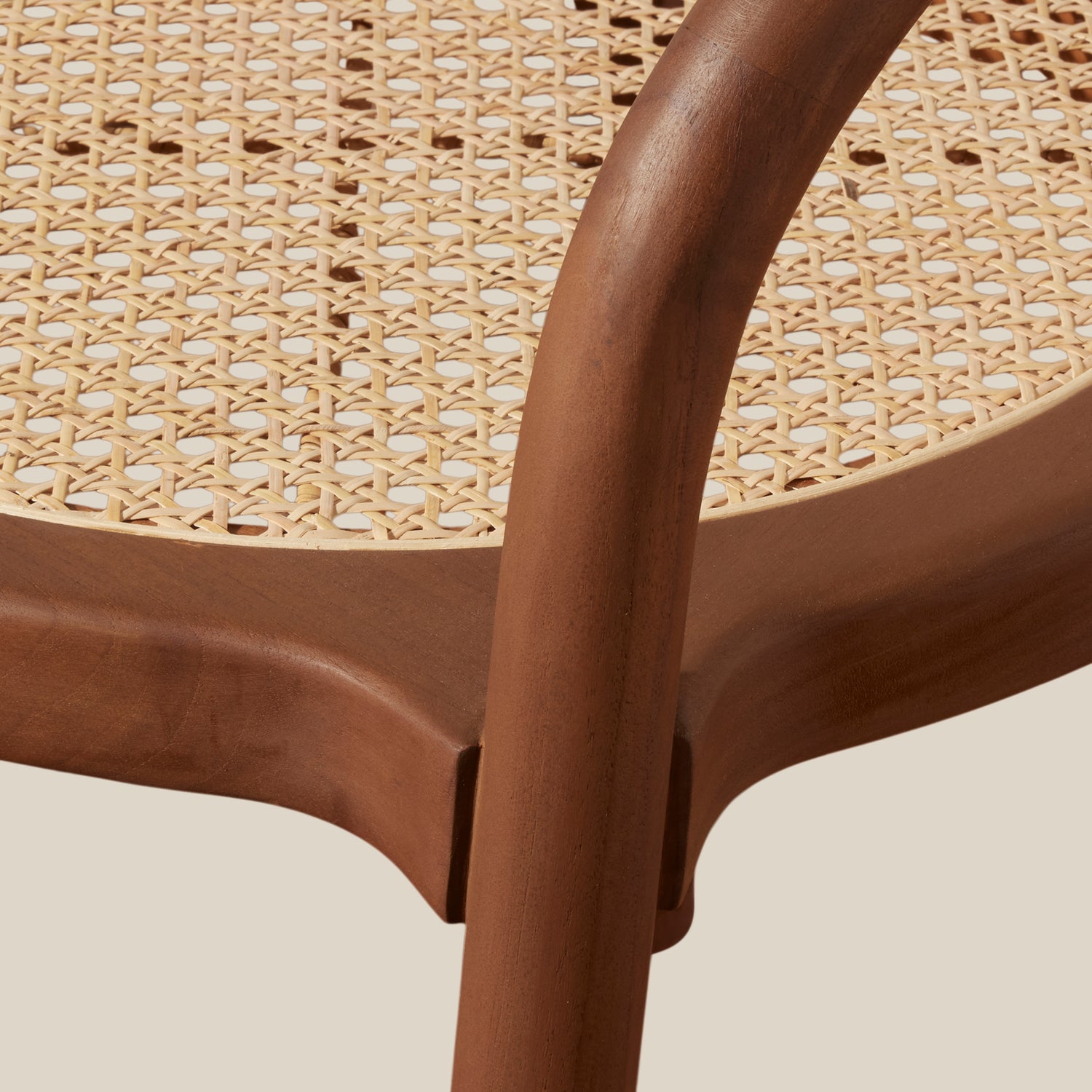 Close-up detail of a modern bistro chair featuring a curved medium-brown wooden frame and a natural woven cane seat, set against a solid light beige background.- Number 6