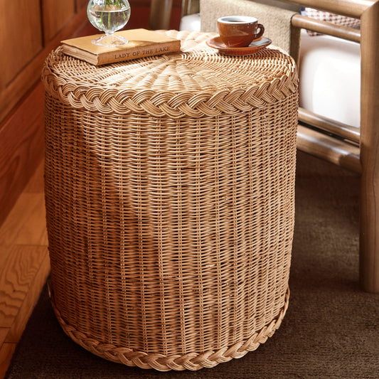 A round woven rattan side table or stool in a warm natural tan color, styled in a cozy room setting with a small glass vase of white flowers and a cup of coffee on top, next to a wooden chair with white cushions. - Image 2