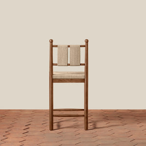 A wooden barstool with a woven beige seat and backrest, set against a solid beige wall and a terracotta hexagonal tile floor. - Number 5