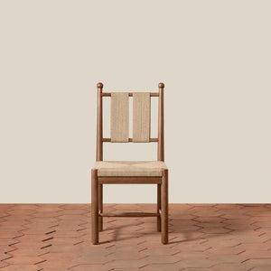 A wooden dining chair with a woven beige seat and backrest, centered against a solid beige wall and a terracotta hexagonal tile floor. - Number 13