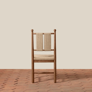 A wooden dining chair with a woven beige seat and backrest, set against a solid beige wall and a terracotta tile floor. - Number 14