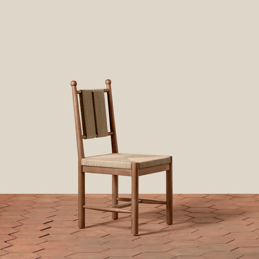 A wooden dining chair with a woven cane backrest and a light beige upholstered seat, set against a solid beige wall and a terracotta hexagonal tile floor.