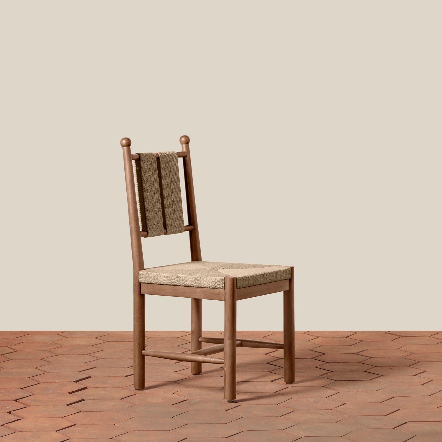 A wooden dining chair with a woven cane backrest and a light beige upholstered seat, set against a solid beige wall and a terracotta hexagonal tile floor.- Number 9