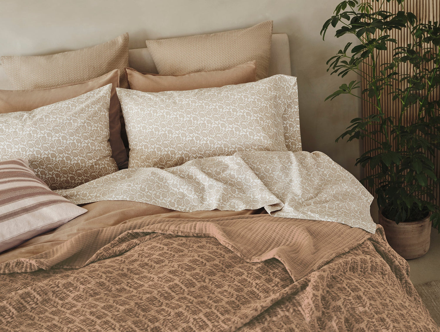 Neatly made bed with patterned bedding and pillows in a cozy room.- Number 2