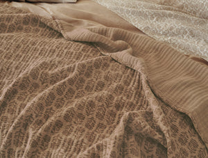 Close-up of a textured brown blanket on a bed with a patterned bedspread. - Number 4