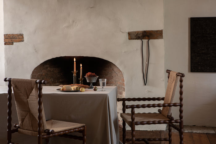 Dining area with a table set against a stone wall, featuring candles and a vase.