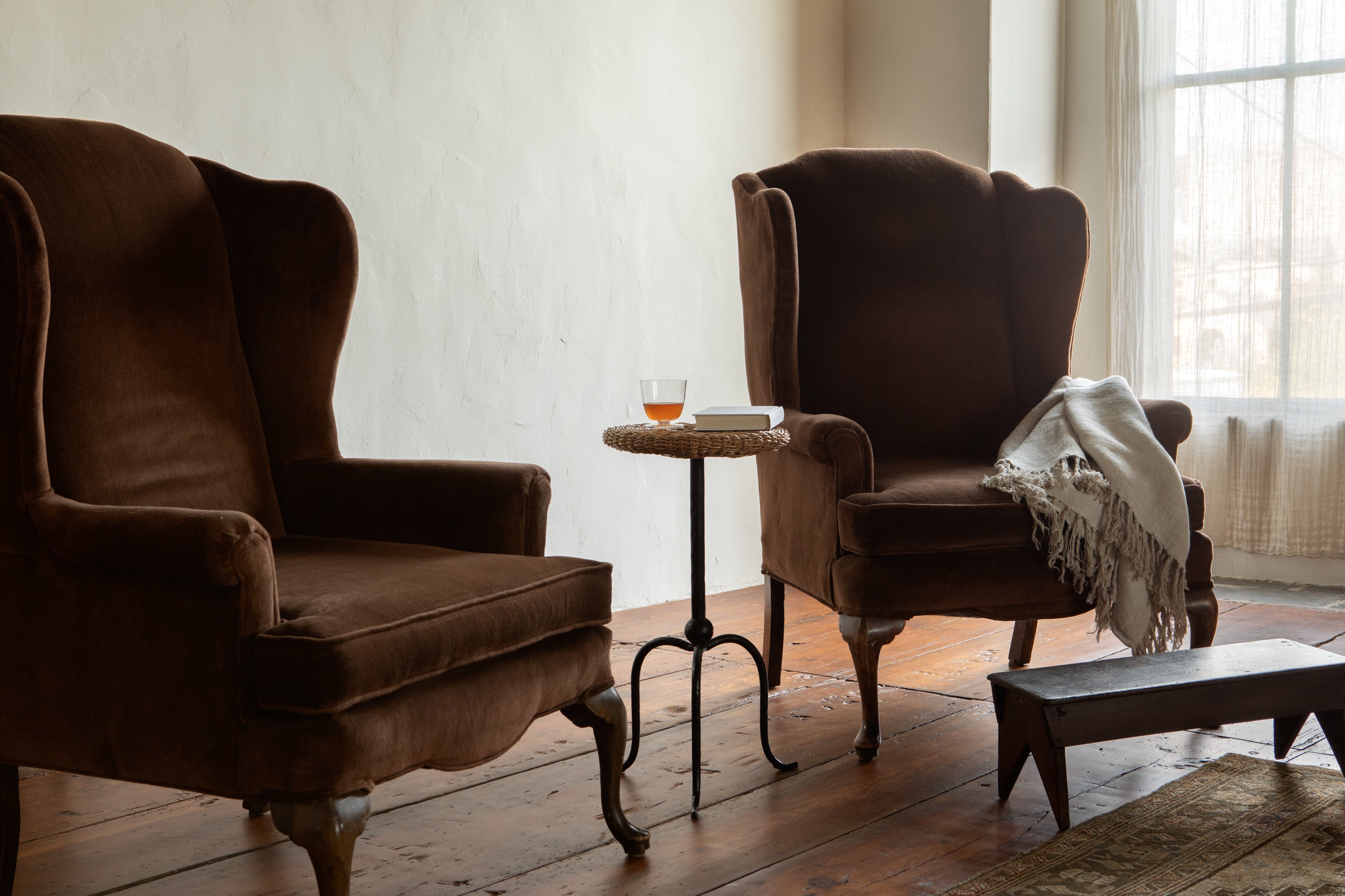 Two brown armchairs in a room with a small table and a blanket.