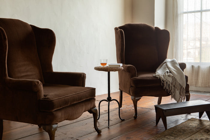 Two brown armchairs in a room with a small table and a blanket.