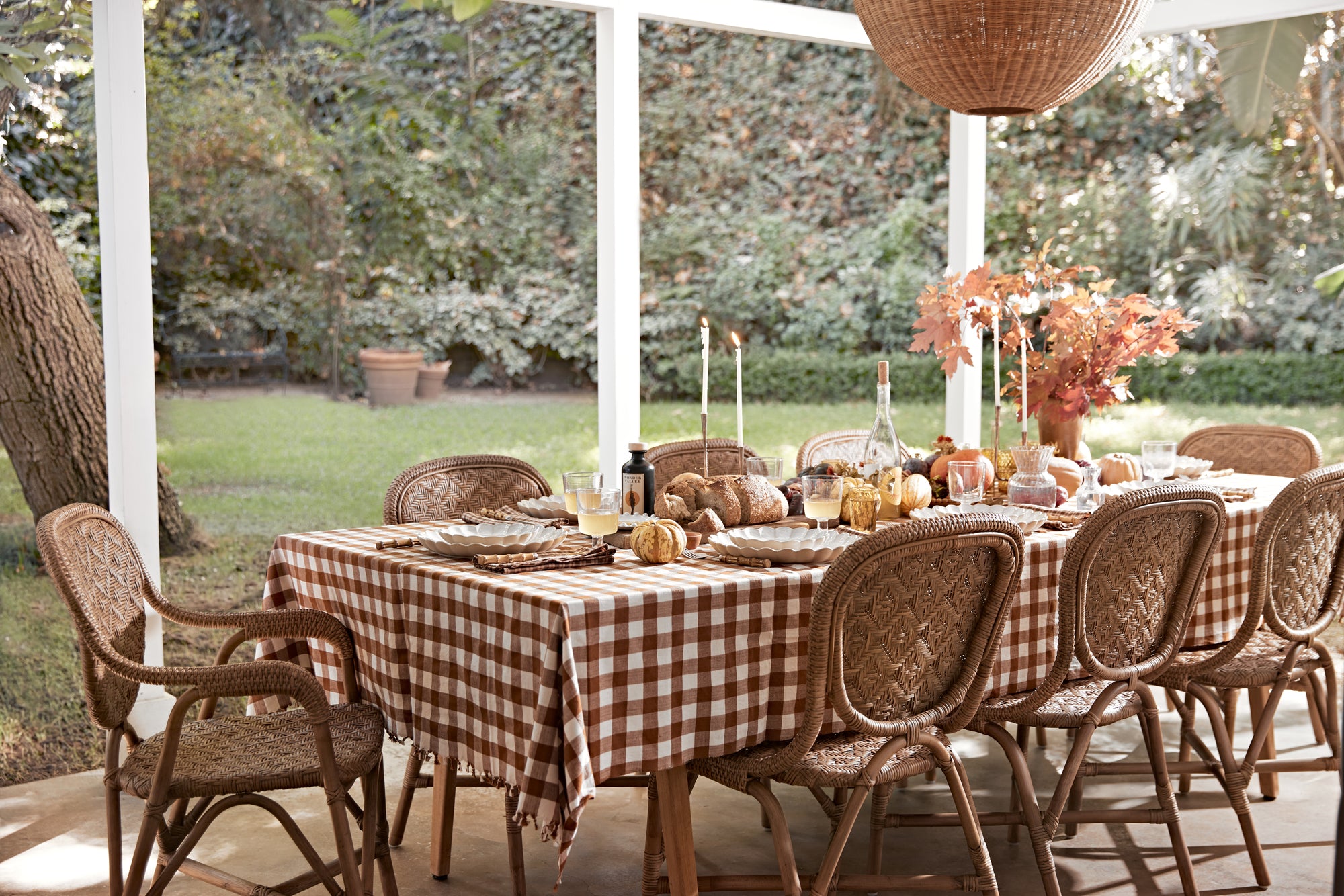 Outdoor dining setup with a checkered tablecloth, pumpkins, and candles on a patio.