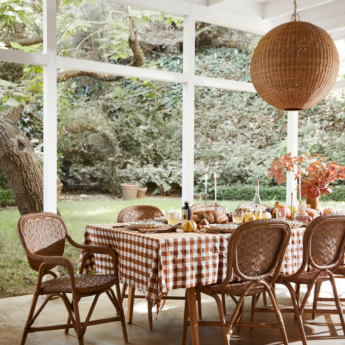 Dining table set with a checkered tablecloth in an outdoor setting with chairs and decorative elements.