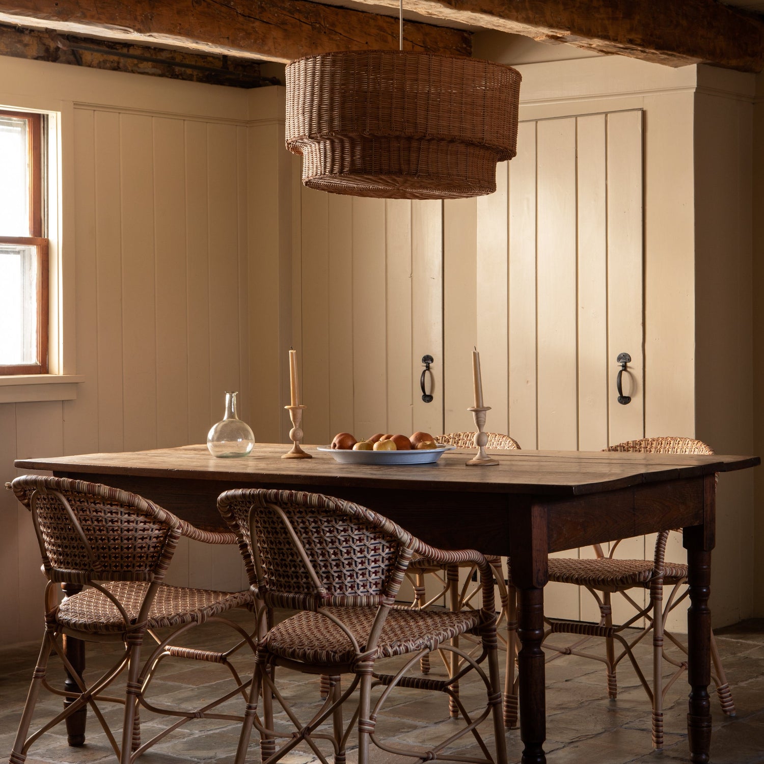 brown woven chairs around a wooden table with woven chandelier above and yellow doors in the background- Number 3