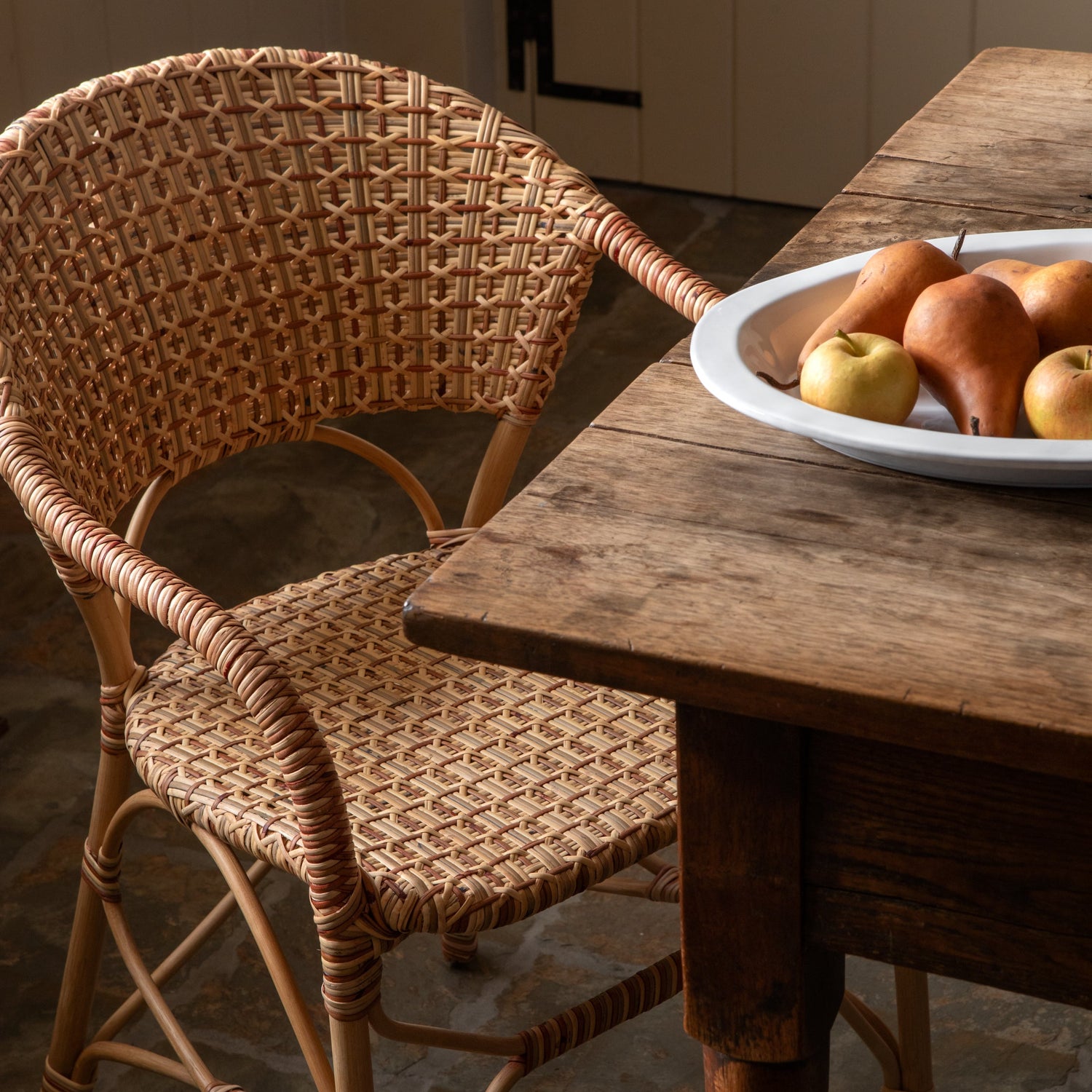 Wicker chair next to a wooden table with a plate of fruit in a kitchen.- Number 2