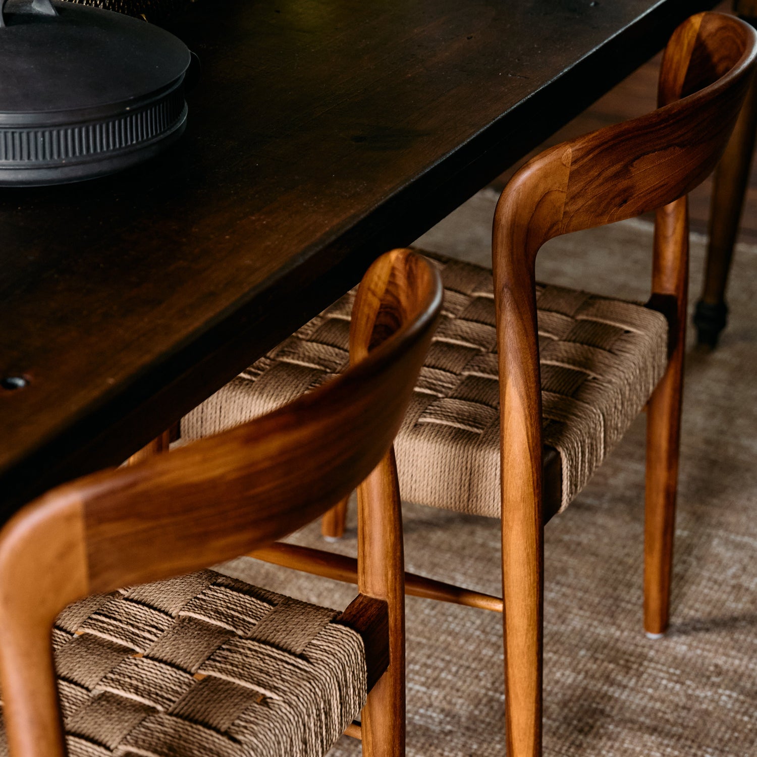 Wooden chairs with woven seats around a dark wooden table on a carpeted floor.- Number 3