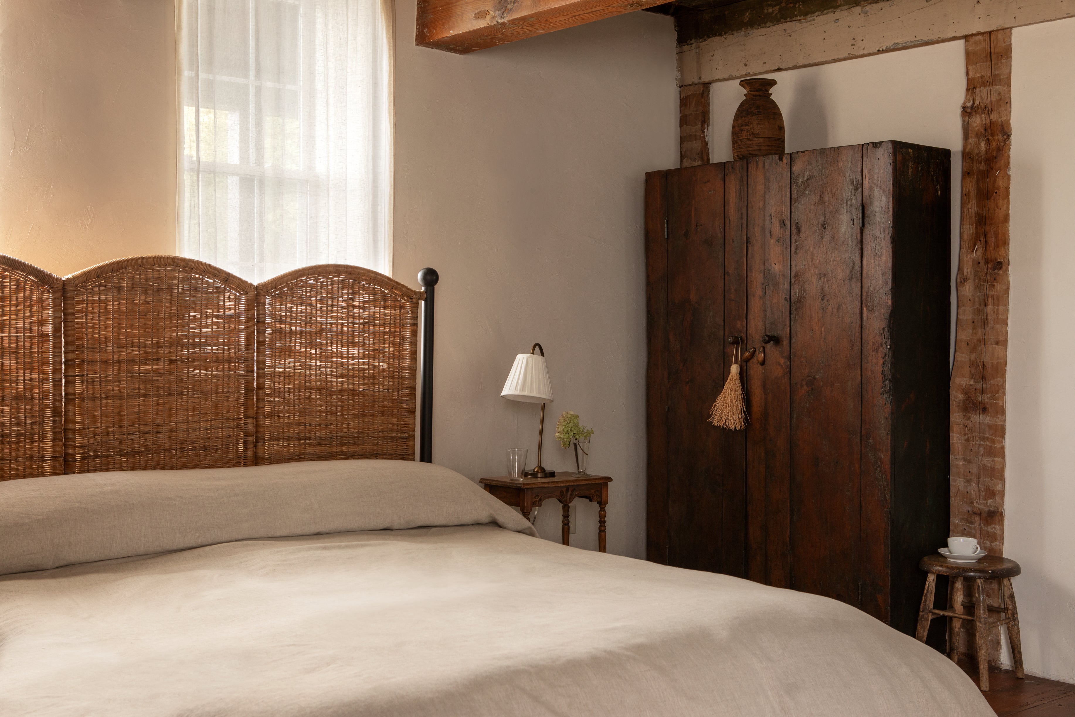 Bedroom with wooden wardrobe, bed with wicker headboard, and small table with lamp.