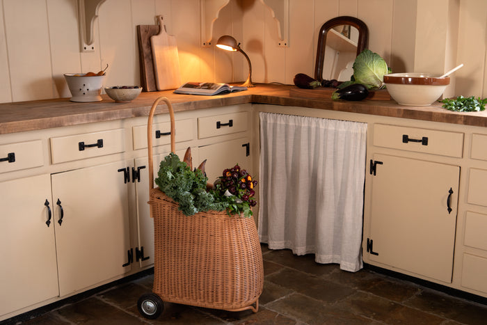 Kitchen with a basket of vegetables on wheels, cabinets, and a countertop.