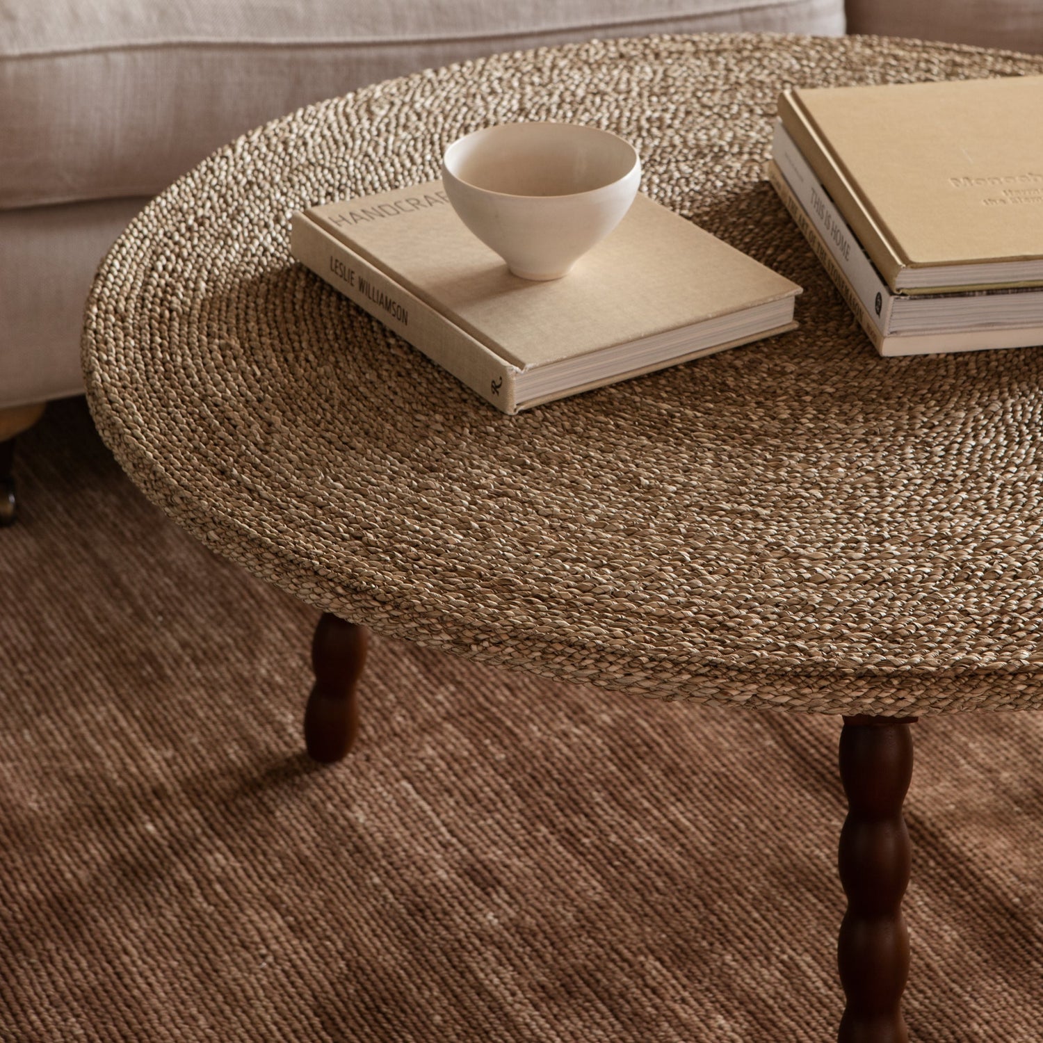 Round woven coffee table with a bowl and books on a beige sofa- Number 3