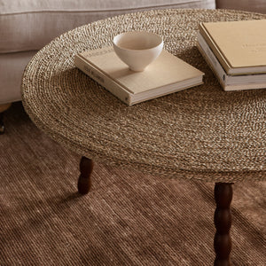 Round woven coffee table with a bowl and books on a beige sofa - Number 3