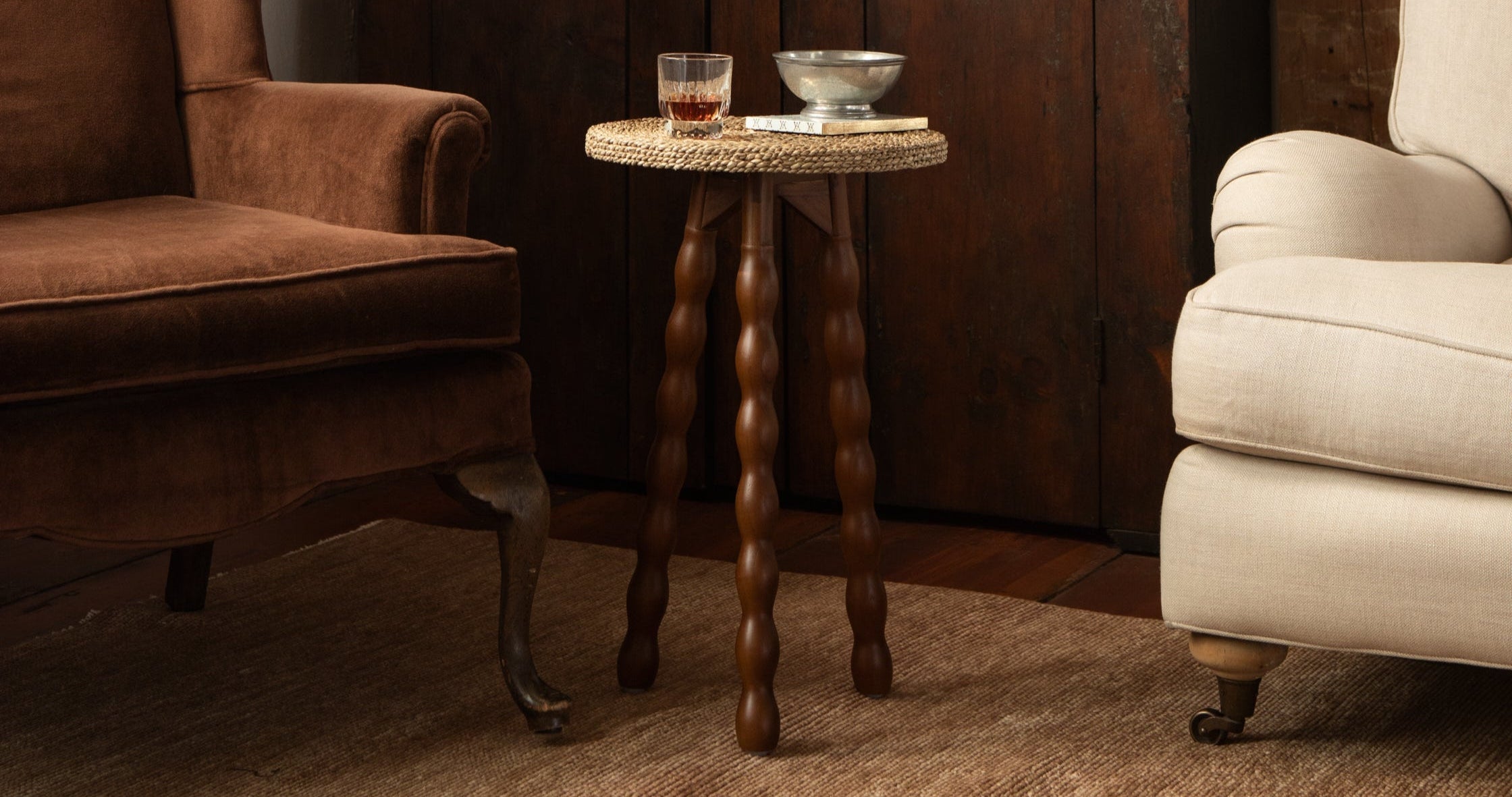 Two armchairs in a room with a wooden side table against a wooden wall.