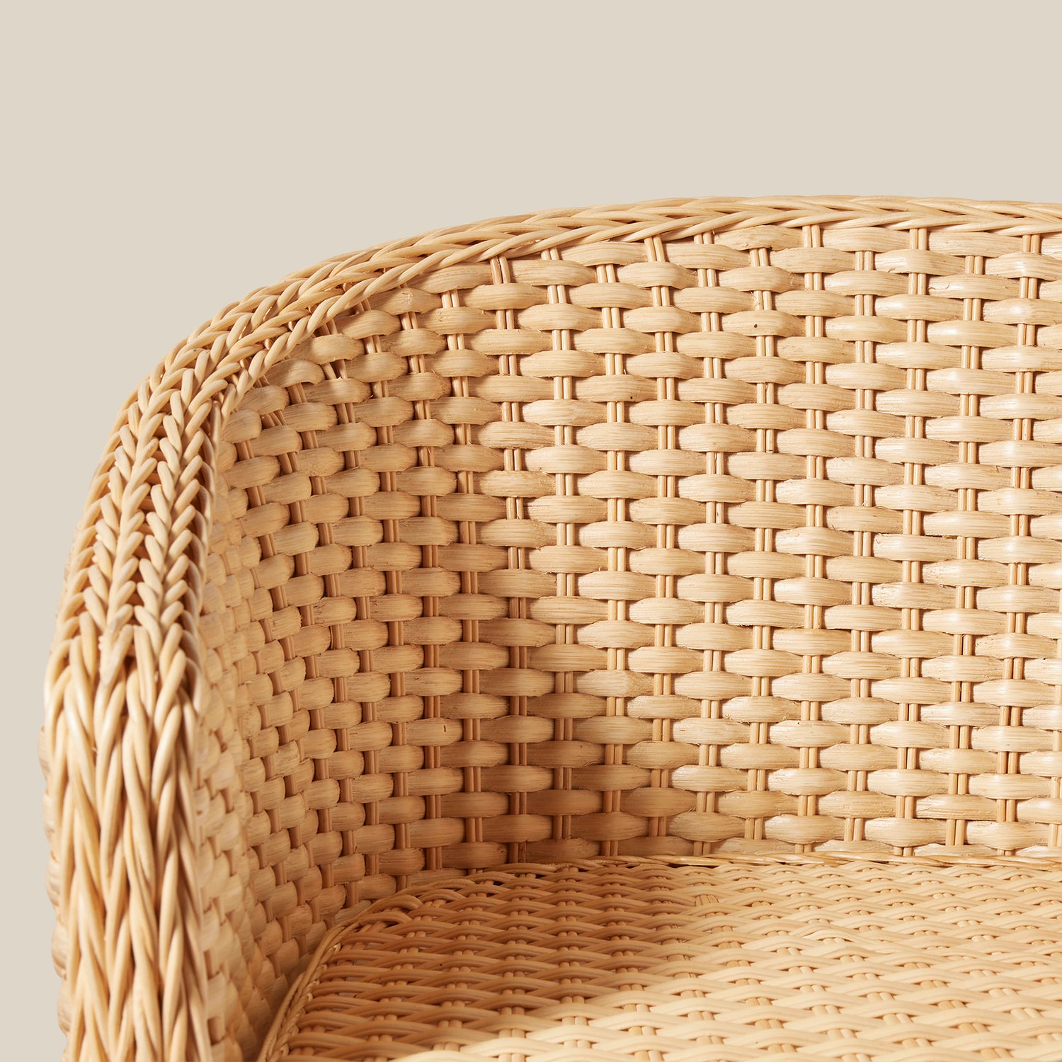 Close-up of a woven rattan chair back and arm in a natural light tan color against a solid light beige background.- Number 7