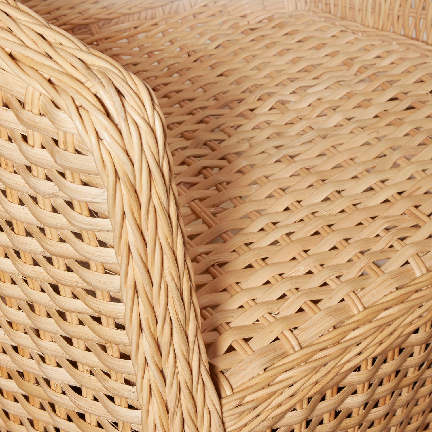 Close-up of a woven rattan chair or basket seat showing the natural light tan woven texture and curved armrest edge.- Number 8
