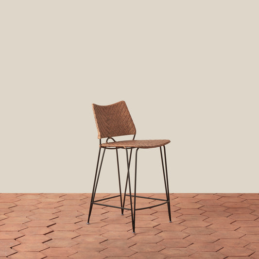 Bar stool with woven seat and backrest on a wooden floor.