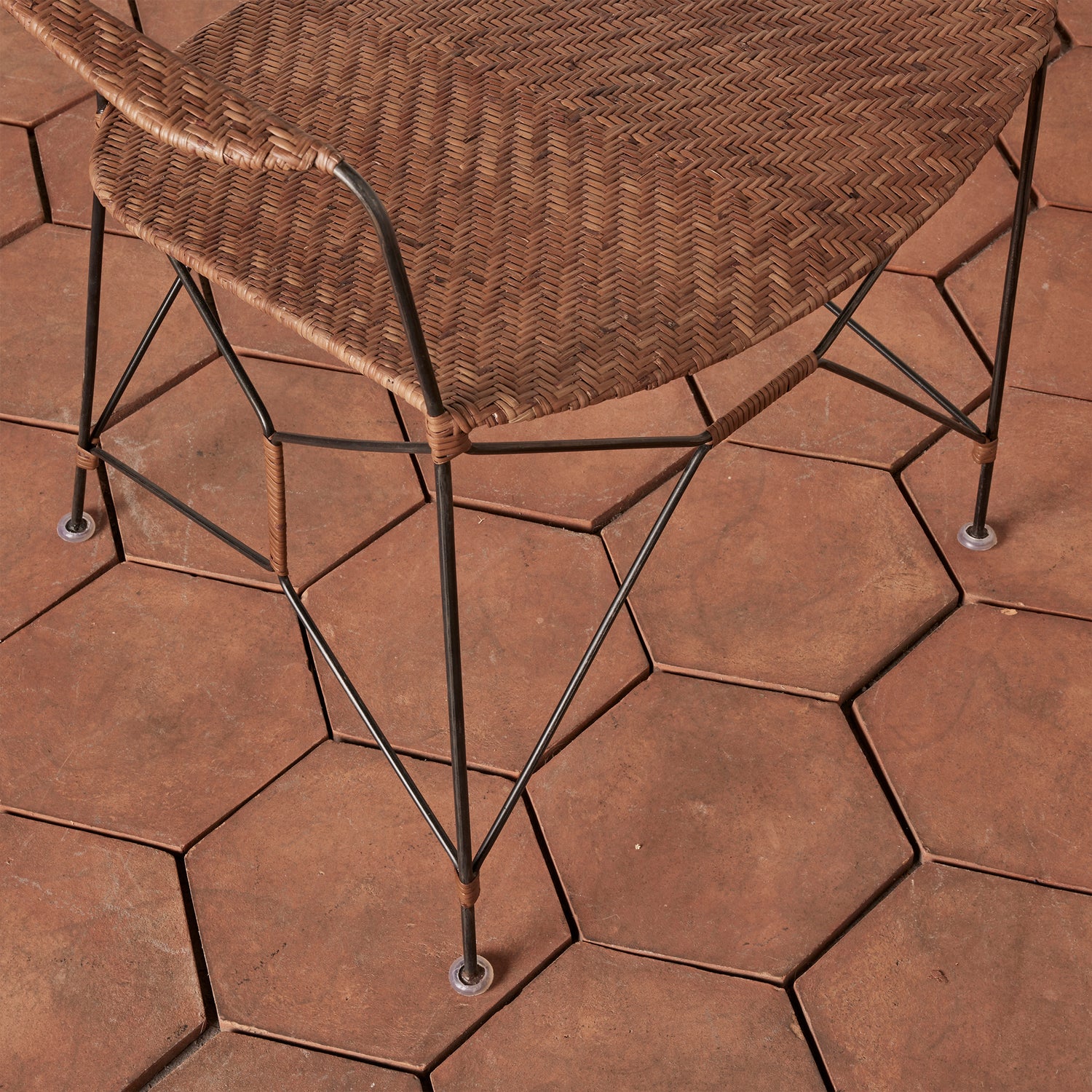 close up of a brown rattan and iron chair seat with pointed legs on tile floor- Number 5