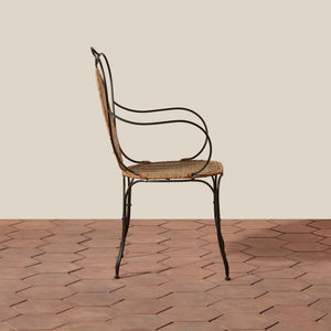 A vintage-style metal and cane armchair shown from the side, positioned on a terracotta tiled floor against a solid beige background. - Number 4