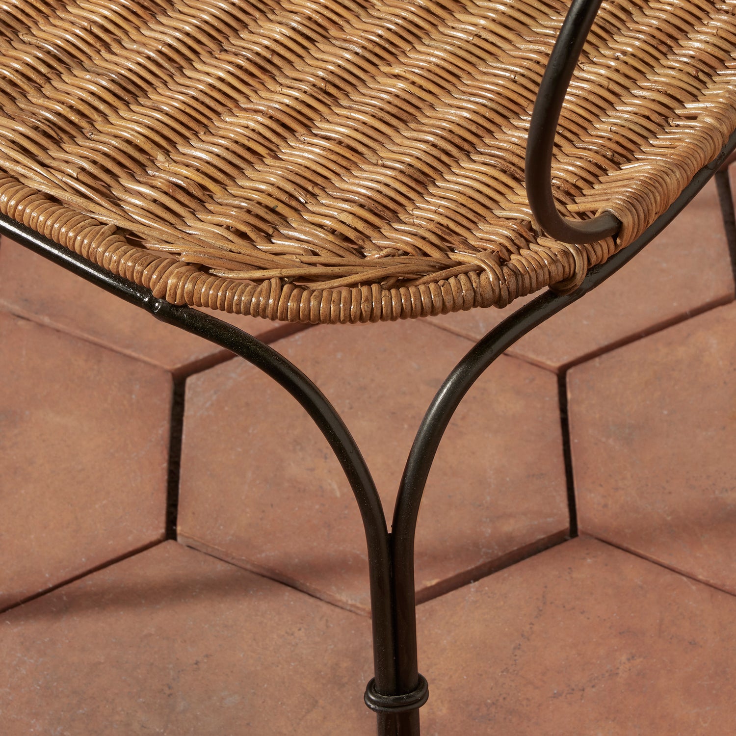 Close-up of a woven wicker or rattan tabletop with a dark metal frame, shown on terracotta tiled flooring.- Number 8