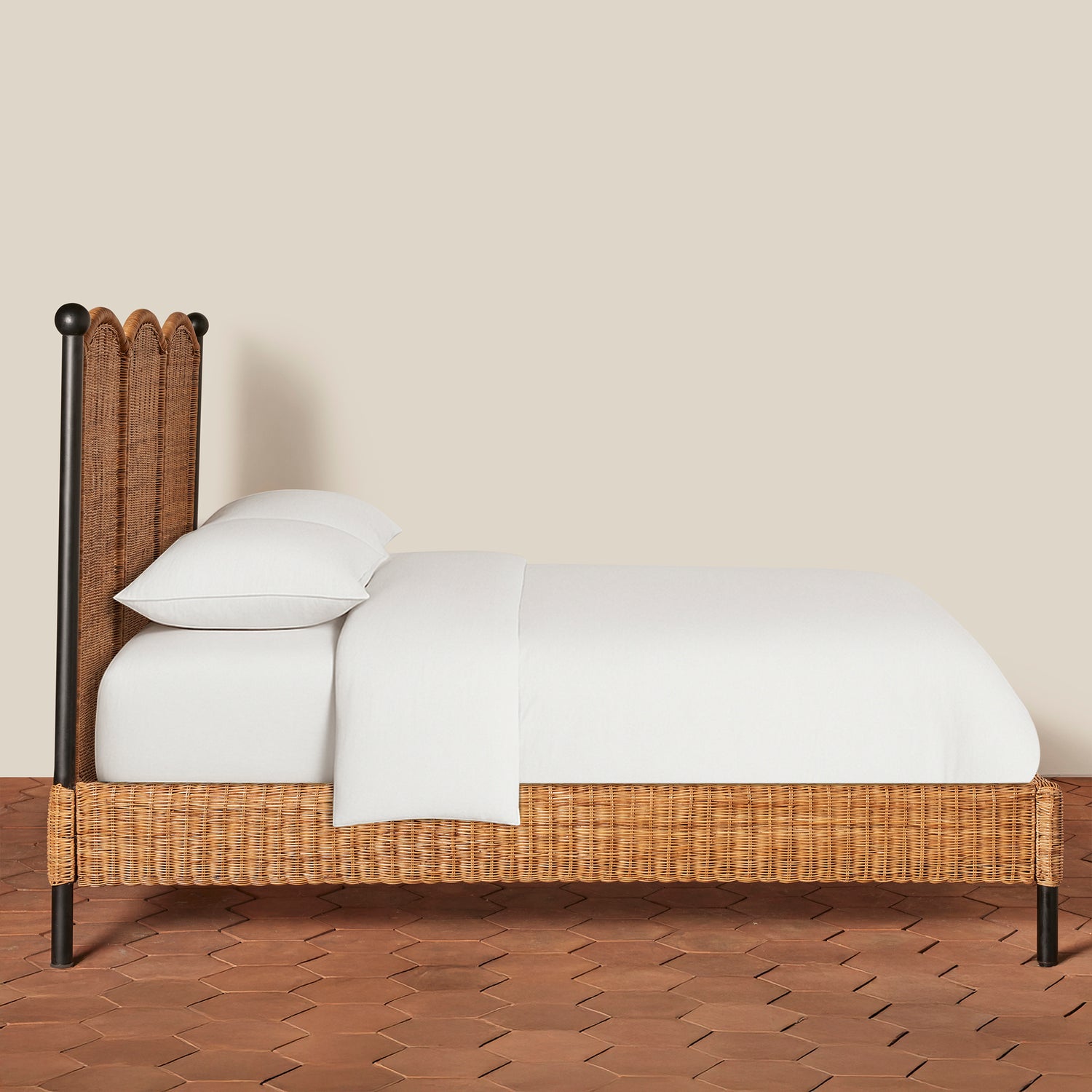 Wicker bed with white bedding on a wooden floor against a beige wall- Number 4