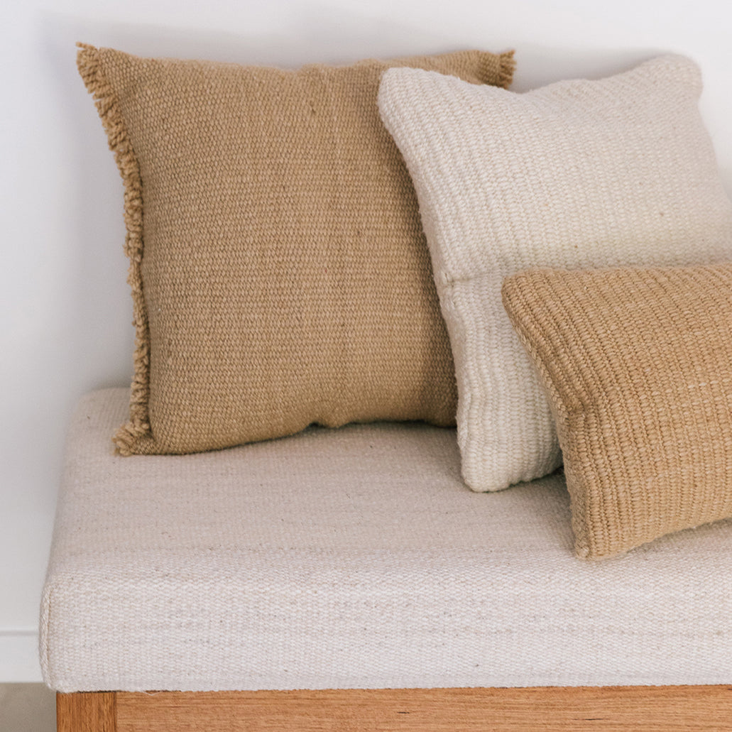 Three textured pillows on a beige cushion against a white wall- Number 3