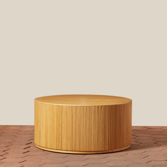 Round wooden coffee table on a wooden floor with a beige wall background