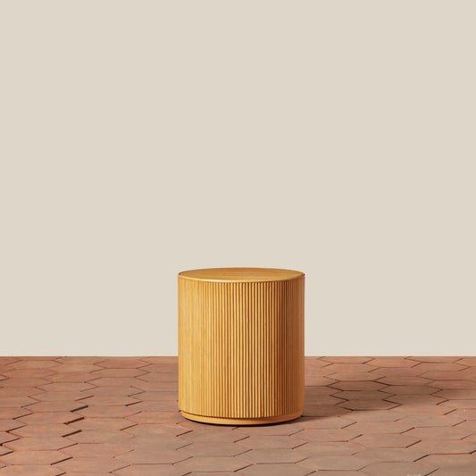 Wooden cylindrical side table on a wooden floor with a beige wall background