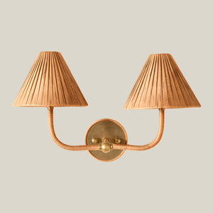 A two-light wall sconce with pleated beige shades and a warm brass metal frame, shown against a solid light gray background. - Number 1
