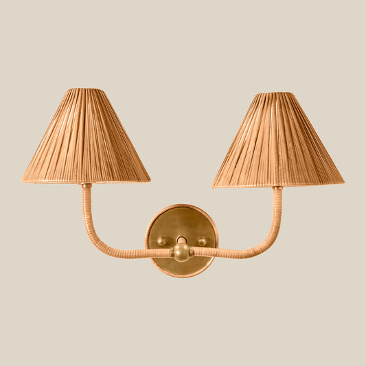 A two-light wall sconce with pleated beige shades and a polished brass wall mount and curved arms, shown against a solid light beige background. - Image 2