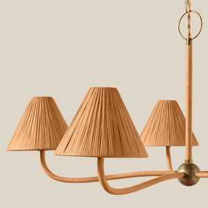 A close-up of a modern chandelier with three pleated conical shades in a warm tan color, attached to curved brass arms and a hanging rod against a solid light beige background. - Number 3