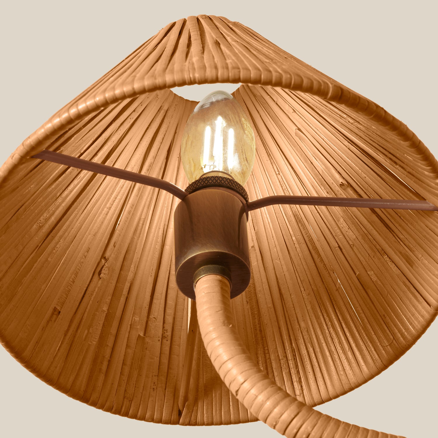 A close-up of a pendant light fixture with a large conical woven shade in a warm tan or light brown tone, a visible clear bulb, and a central dark metal socket with a curved cord extending downward, set against a plain light beige background.- Number 5
